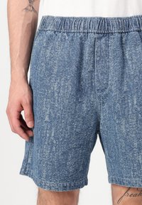 Shorts de estilo denim en un tono azul claro con una textura desgastada. Cuentan con una cinturilla elástica y bolsillos laterales.