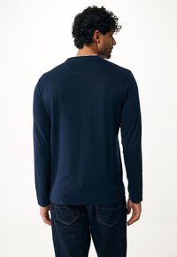 Camicia a maniche lunghe blu navy realizzata in tessuto morbido, con scollo rotondo e un sottile dettaglio di cucitura sul retro. Indossata con jeans scuri.