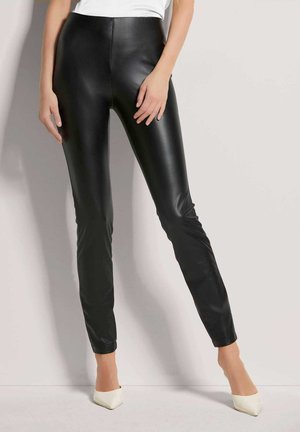 Zwarte nepleer legging met een hoge taille, gladde textuur en slim-fit ontwerp. Gecombineerd met witte spitse hakken.