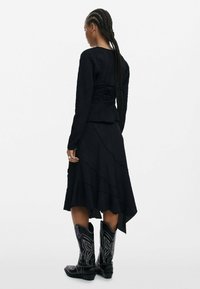 Black textured dress with layered hem and a cinched back, paired with black cowboy boots featuring white decorative stitching.