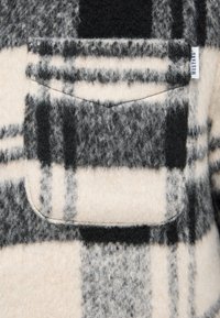 Wool blend shirt with a black and cream plaid pattern. Features a chest pocket with unbrushed texture and soft, fuzzy finish.