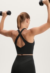 Čierny športový crop top s pretekárskym strihom, s výrezom na chrbte. V kombinácii s čiernymi legínami s vysokým pásom a textúrovanými akcentmi.