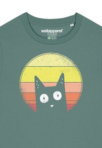 Cyan t-shirt met een ronde afbeelding van een zwarte kat tegen een gestreepte achtergrond in geel, oranje en roze, met een gestructureerd ontwerp.