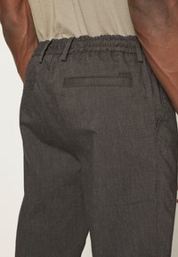 Svarta, vävda byxor med elastisk midja och sidofickor. Har en enkel design och en slät yta. Bakfickan är synlig.