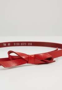 Cintura in pelle rossa con una texture liscia e un design annodato. Marcature all'interno mostrano la taglia e il codice del prodotto.