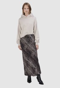 Beige oversized hoodie met een trekkoord, gedragen met een lange, jurk met luipaardprint. Zwarte enkellaarsjes maken de outfit af.