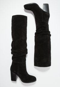Bottes noirs en daim montant au-dessus du genou avec un design ample, un talon bloc haut et une texture lisse, dotées d'un bout arrondi et de coutures nettes.