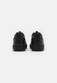 Svarte Nike-sneakers med glatt skinnmateriale, rund design, teksturerte detaljer og en logo preget på hælen.