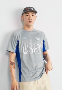 Šedé a modré sportovní tričko s krátkým rukávem, na přední straně s velkým bílým grafikou "OBEY!", hladký povrch a volný střih.