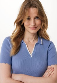 Ljusblå randig polo t-shirt med kort ärm, scalloperade fållar och vita detaljer vid kragen. Subtil textur och figurnära design.