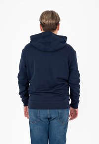 Felpa blu navy realizzata in tessuto morbido, con cappuccio regolabile e polsini a coste, abbinata a jeans blu chiaro. Texture liscia, senza motivi visibili.