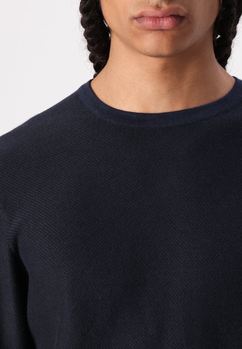 Navyfarbener Pullover mit strukturiertem Strick, mit Rundhalsausschnitt und dezenten Rippdetails an den Bündchen und dem Saum, aus einem weichen Stoff gefertigt.