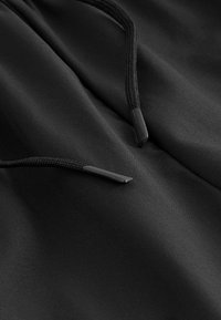 Tissu noir à texture lisse présentant deux cordons noirs, chacun avec une extrémité en plastique arrondie, partiellement visibles sur le matériau.