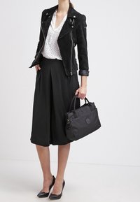 Mustapaarasta nahkatakki valkoisen pilkullisen paidan päällä, yhdistettynä mustaan midi-hameeseen, mustiin korkokenkiin ja teksturoituun mustaan käsilaukkuun.