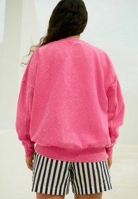 Oversize lyserød sweatshirt med en blød tekstur og ribbet manchetter, kombineret med marineblå og hvide stribede shorts. Løs pasform.