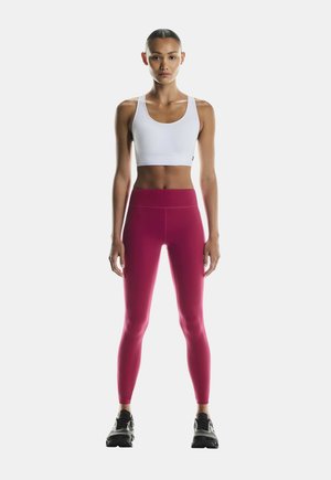 Valge sportlik lühike topp, milles on kõrge talje ja sobivad säravad roosad leggings, millel on sile tekstuur ja minimalistlik disain.