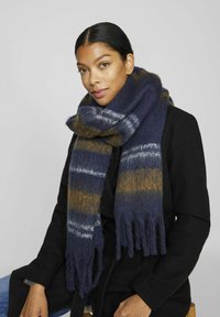 Écharpe rayée bleu marine et marron en matériau doux et moelleux, avec des extrémités à franges et un design épais et confortable. Portée autour du cou.