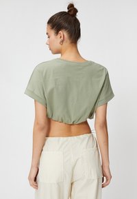 Kortærmet olivengrøn cropped t-shirt med rund halsudskæring og opsmøgte ærmer, båret med lyse højtaljede bukser.