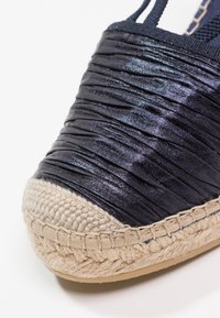 Espadrille en tissu navy avec une texture froncée, un capuchon de orteil en jute rond et des détails tressés le long de la semelle. Fabriquée à partir de matériaux flexibles.