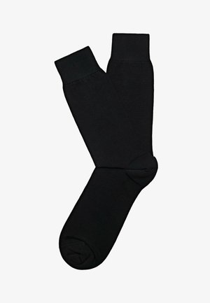 Ein Paar schlichte schwarze Crew-Socken liegen flach auf weißem Hintergrund, überlappen sich an den Knöcheln, Zehen und Bündchen sind sichtbar.