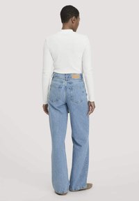 Vaaleansiniset korkeavyötäröiset, leveälahkeiset farkut, joissa on kulutettu pinta. Sisältää paikkataskun ja merkin takavyötäröllä.