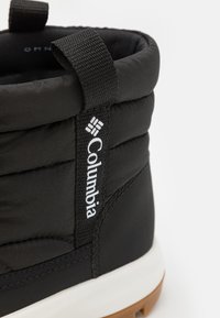 Črne tople škornje z oblazinjeno zgornjico, tkaninskim trakom za nošenje in belim logotipom "Columbia". Imajo gumijast podplat za oprijem in vzdržljivost.