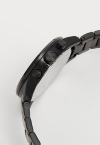 Montre chronographe en métal noir avec un boîtier circulaire lisse, des boutons-poussoirs texturés et un bracelet en maillons métalliques. Le cadran est minimaliste et sans marquage.