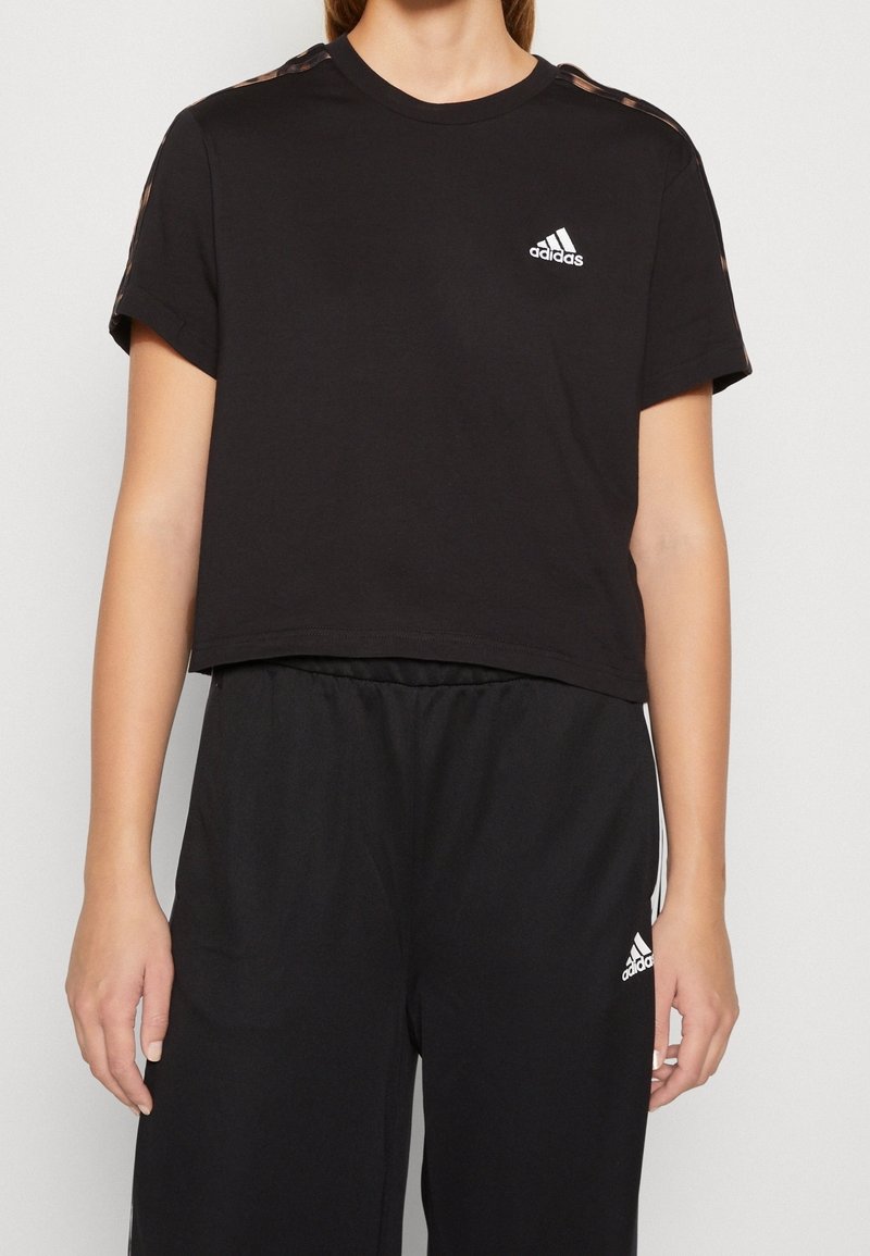 Černé zkrácené tričko vyrobené z bavlny, s krátkými rukávy, kulatým výstřihem a bílým logem Adidas na hrudi.