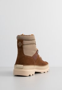 Brown suede ankle boots with a beige padded collar, orange laces, and a chunky cream sole. GANT logo on the back.