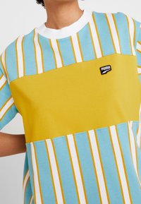 Färgglad randig t-shirt med ljusblå, vit och gul panel. Tillverkad av bomull med rund halsringning och liten svart logotypdetalj.