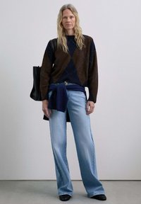 Maglione a losanghe marrone e blu navy, jeans in denim azzurro chiaro morbidi e borsa nera. I jeans sono a vita alta con gamba dritta. Scarpe nere completano l'outfit.