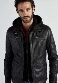 Zwarte leren jack met een capuchon, voorzien van ritszakken en een nauwsluitend ontwerp. Het materiaal heeft een gladde textuur en een subtiele glans.