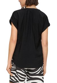 Schwarzes T-Shirt mit kurzen Ärmeln und gewellter Oberfläche, Faltendetail im Rücken und umgeschlagenen Ärmeln, kombiniert mit weißen Shorts im Zebra-Stripe-Design.