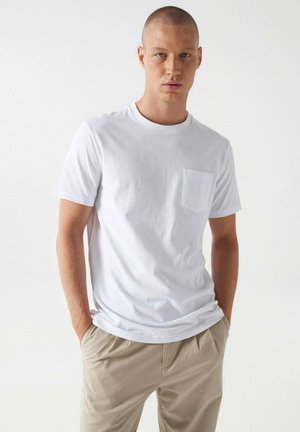 Camiseta de algodón blanca con cuello redondo y mangas cortas, que presenta un pequeño bolsillo en el pecho y una textura lisa y uniforme.