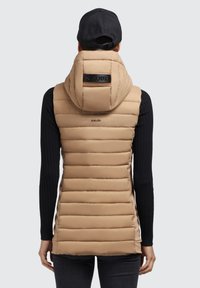 Gilet imbottito beige con colletto alto e cappuccio. Design a righe verticali, texture morbida, marchio nero sulla schiena, abbinato a un top nero con maniche lunghe.