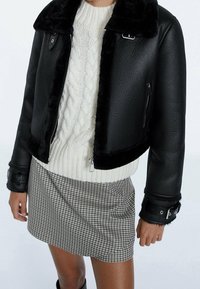 Personne portant une veste en cuir de mouton noir, un pull en maille blanche et une jupe mini à carreaux, vue du cou à mi-thigh.