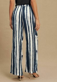 Flowy, wide-leg pants with a crinkled texture, navy and white vertical stripes, and a high waist design. Paired with pointed-toe sandals.