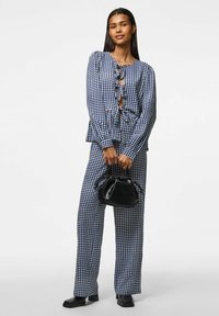 Marinblå och vit rutigt tvådelat set med långa ärmar, knappdetaljer och vida byxor; matchat med en liten svart handväska.
