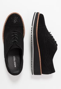 Chaussures oxford en daim noir avec détails perforés, semelle plate en caoutchouc et couture contrastante brun sur les bords.