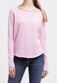 Ljusrosa långärmad topp med båtformad halsringning och rå kant, bärs över mörkblå jeans. Mjuk, texturerad tyg.