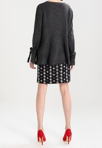 Maglione oversize grigio con dettagli a cravatta sulle maniche, abbinato a una gonna a righe bianco e nero. Scarpe rosse con tacco alto completano l'outfit.