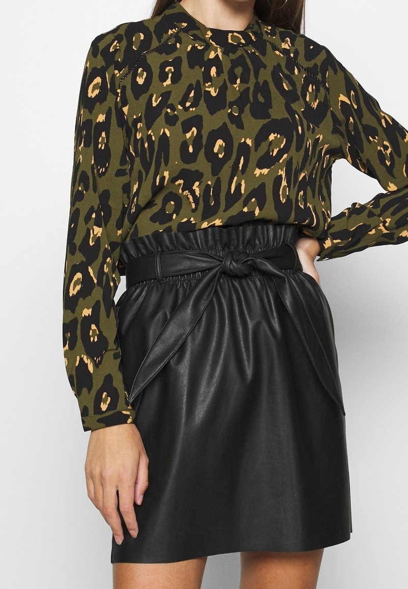 Blusa a maniche lunghe verde oliva con stampa leopardata nera e beige; abbinata a una gonna nera in ecopelle con dettaglio della cintura annodata.