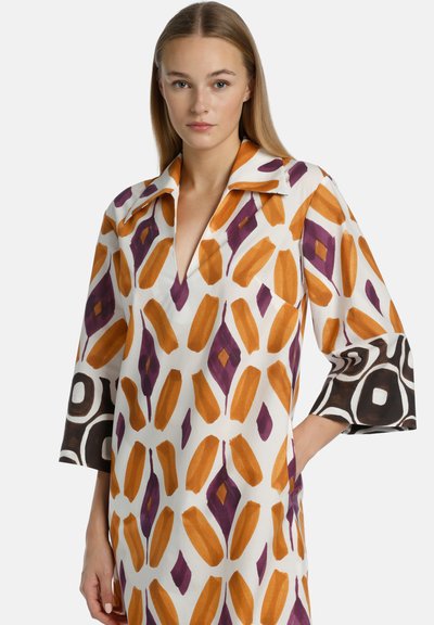Abito a maniche lunghe in un tessuto bianco con motivi geometrici arancioni e viola, con polsini a contrasto in bianco e nero.