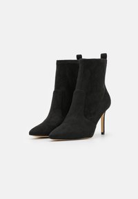 Pair of black suede ankle boots with pointed toes and thin high heels on a white background.