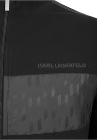 Czarna kurtka na zamek z teksturowanym panelem z geometrycznymi wzorami. Logo „KARL LAGERFELD” w matowej czerni, umieszczone na piersi.