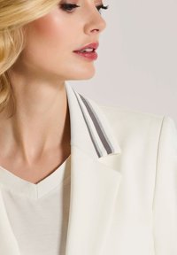 Witte blazer met een contrasterende gestreepte kraag, gecombineerd met een licht v-hals top, gemaakt van soepele stof en een getailleerd ontwerp.
