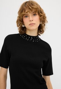 Černý pletený top s krátkými rukávy a zdobeným výstřihem z černých a stříbrných korálků. Hladká textura, přiléhavý střih.