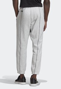 Šedé teplákové kalhoty z měkké tkaniny, s bočními kapsami, elastickým pasem a kontrastním prošitím podél vnějších švů.