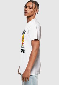 T-shirt en coton blanc avec un graphique de personnage de dessin animé en rouge et jaune, accompagné d'une écriture noire en dessous. Manches courtes, coupe décontractée.