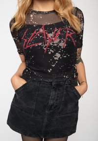 Black mesh T-shirt with red "Slayer" graphic and splatter pattern; paired with a black denim skirt featuring front pockets and a high waist.